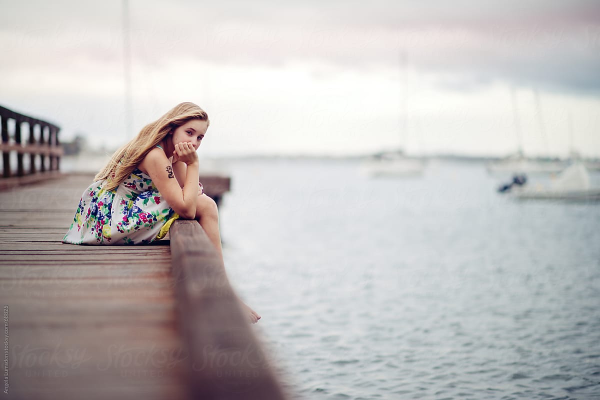 Girl Sitting On A Dock On A Cloudy Day By Angela Lumsden Stocksy United
