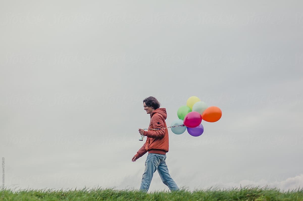 Teenage boy walking in the grass holding a bunch of balloons
