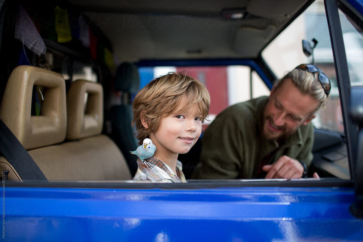 Boy and his dad sitting in campervan while having a bird on his shoulder