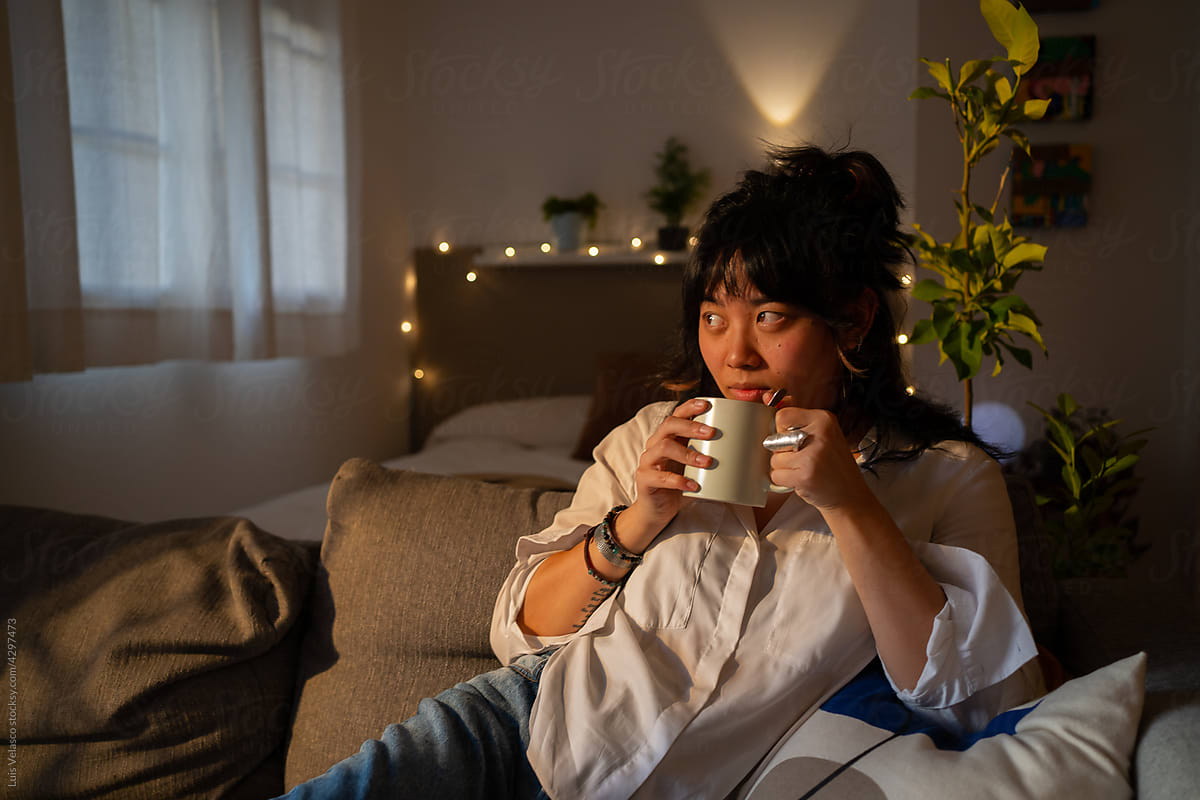 Asian Woman On The Couch At Home Having A Coffee.