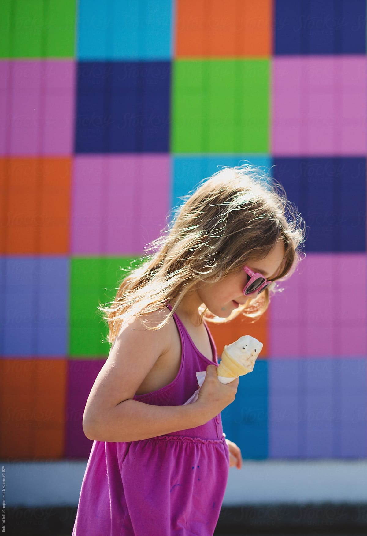 Cute Young Girl Eating Ice Cream Near Colorful Wall In Summer By Rob