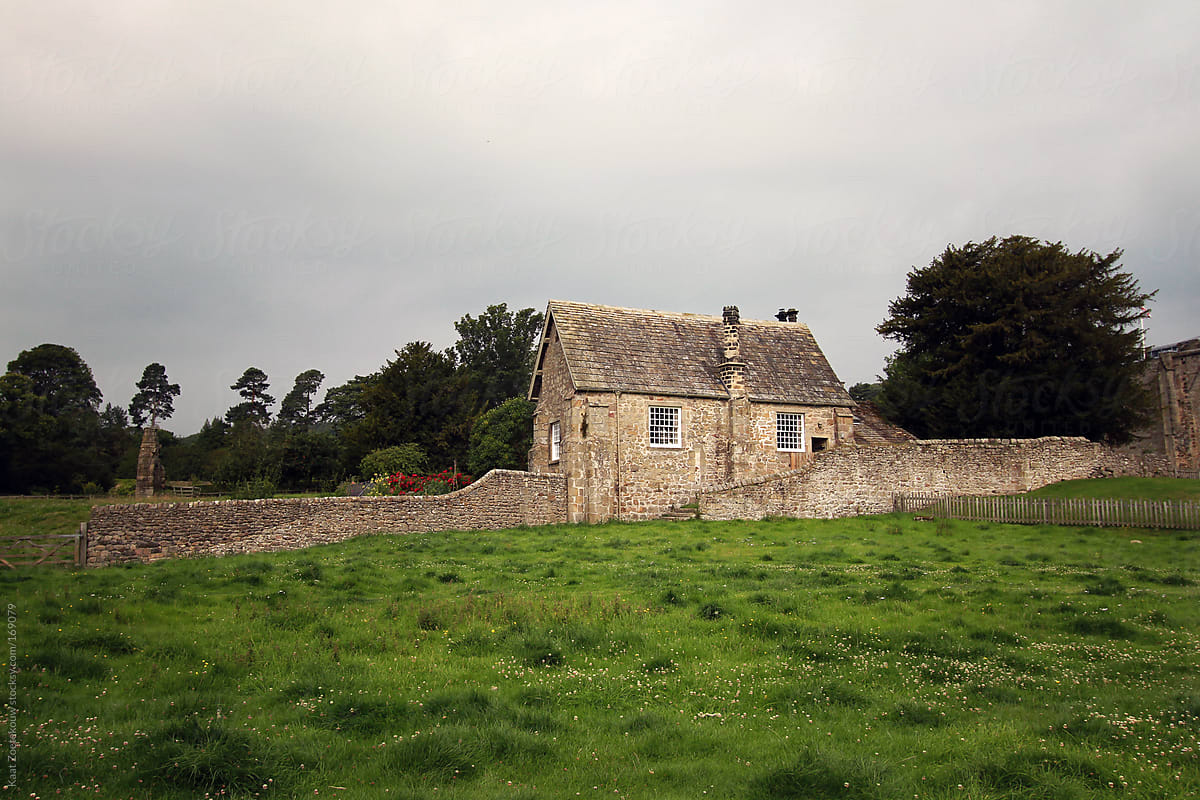 A Yorkshire cottage surrounded by green grassland and trees on a cloudy day.