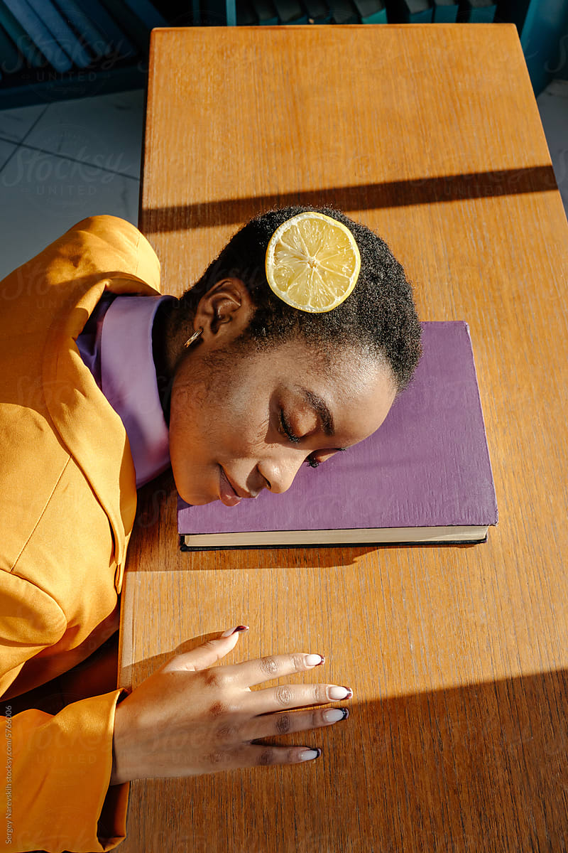 Woman sleeping with head on book, cutted lemon on hair