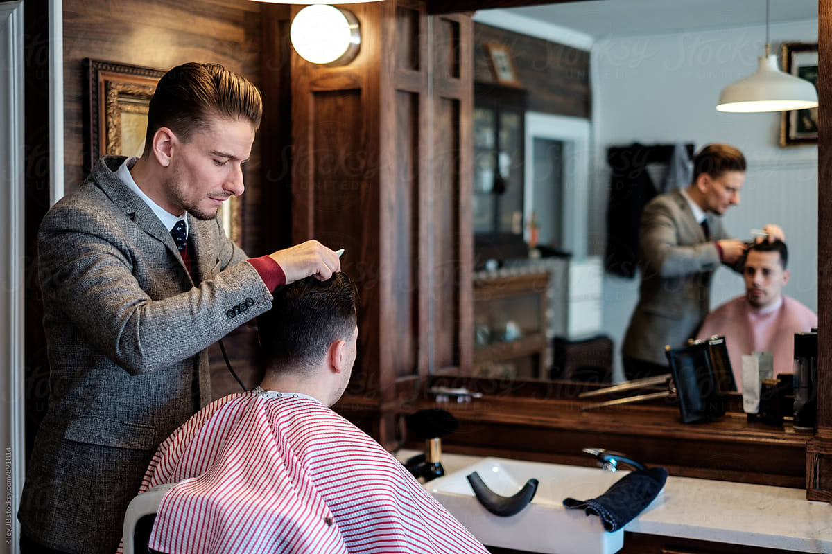 A gentleman barber focuses as he cuts a client's hair.