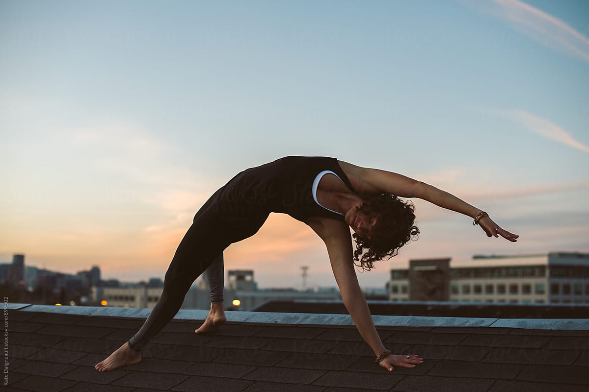 woman doing yoga on city rooftop at dusk.