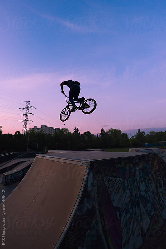 Cyclist silhouette performing midair tricks on ramps during twilight