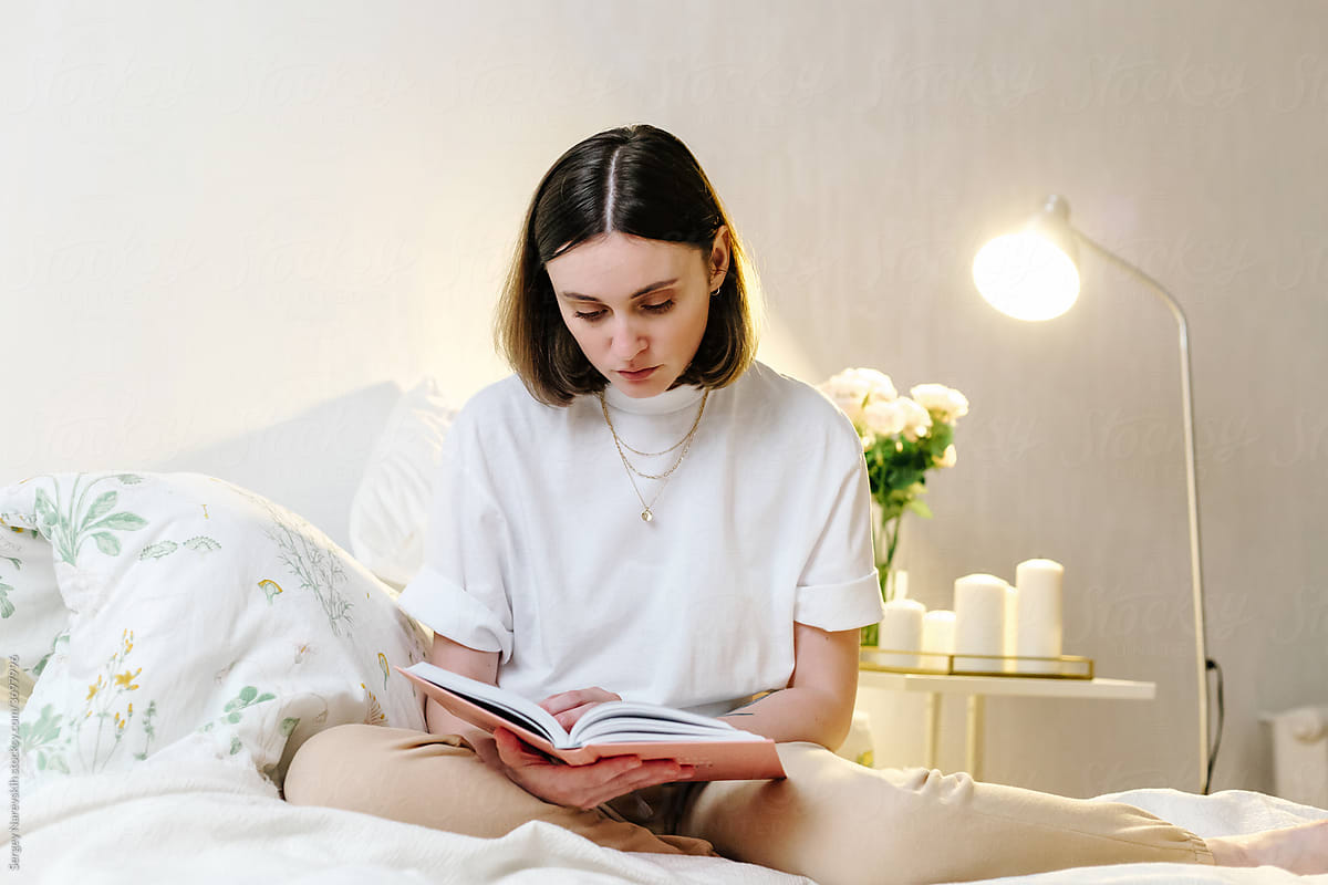 Peaceful woman reading book on bed at home