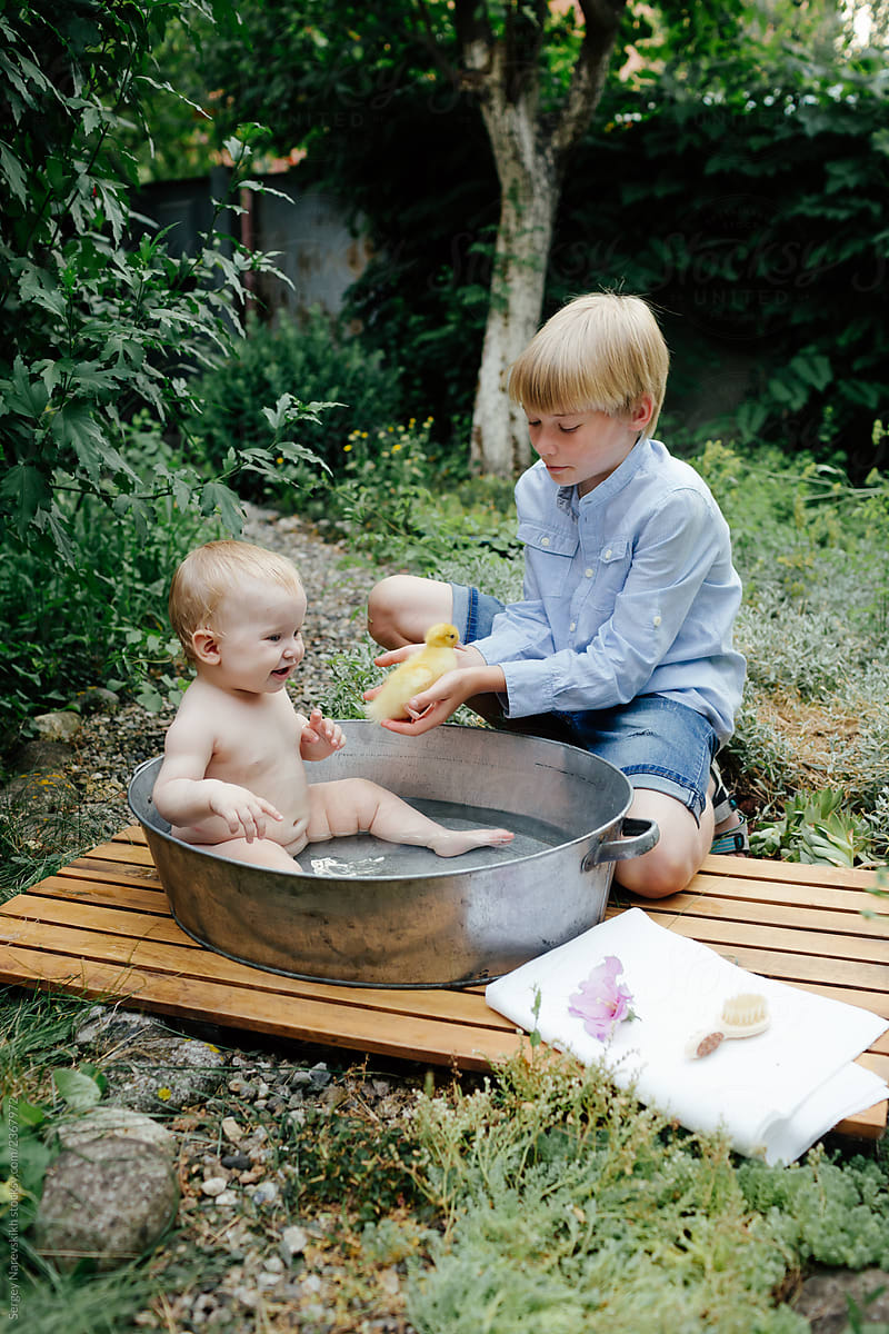 Boy sitting near basin with infant baby and holding duckling