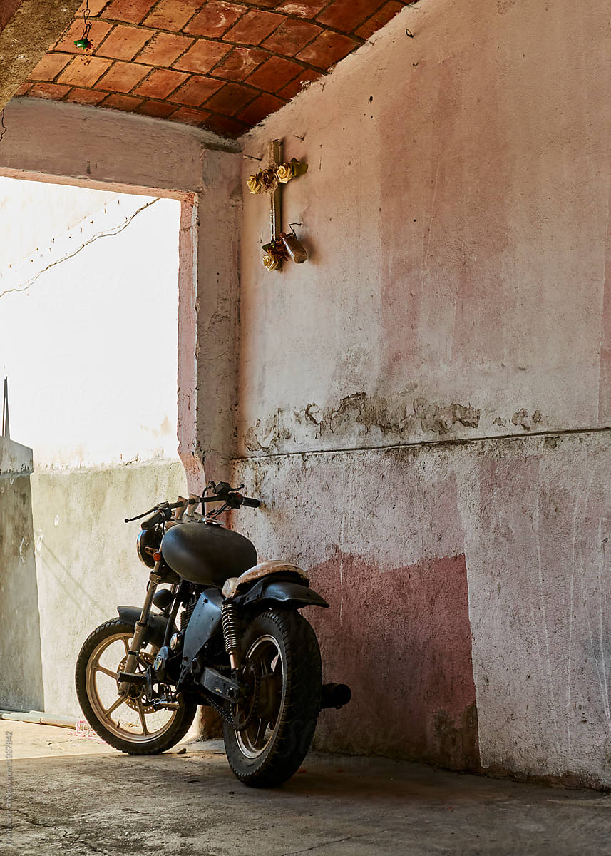 Motorcycle parked along a plaster wall with a cross hanging above