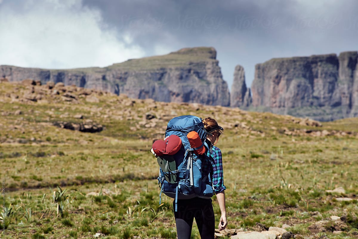 Female hiker with her back pack hiking through a field surrounded by mountains.
