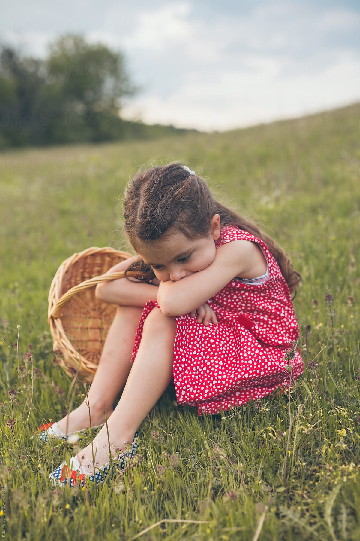 Sad Little Girl Sitting In Grass porDejan Ristovski.