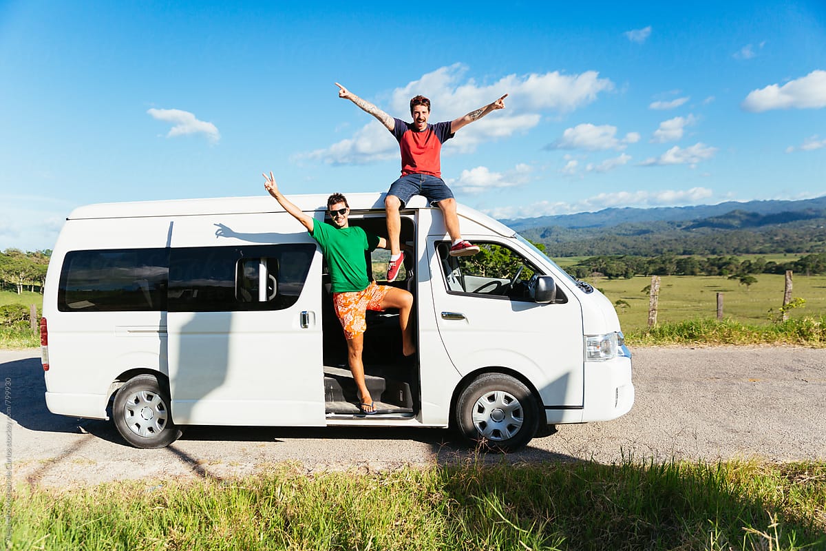 Two excited young men saluting from their white minivan during a break stopover in the middle of the road in the countryside