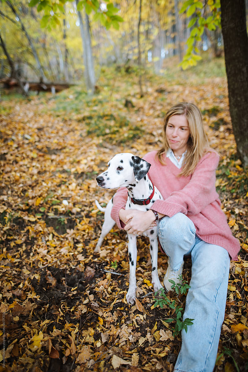 Young woman hugging her dog sitting in autumn park