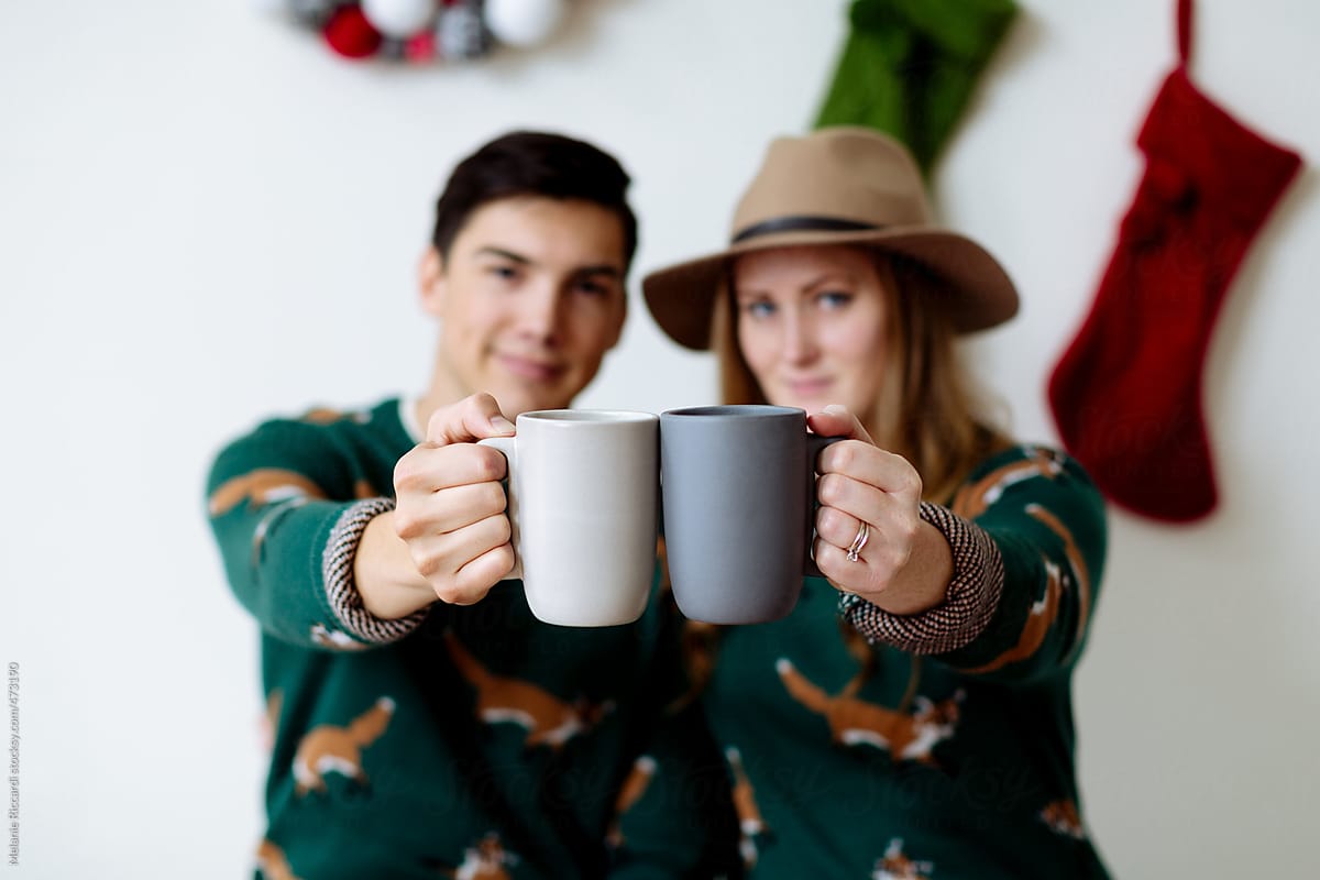 Blurred holiday portrait of a couple cheering with coffee mugs in focus