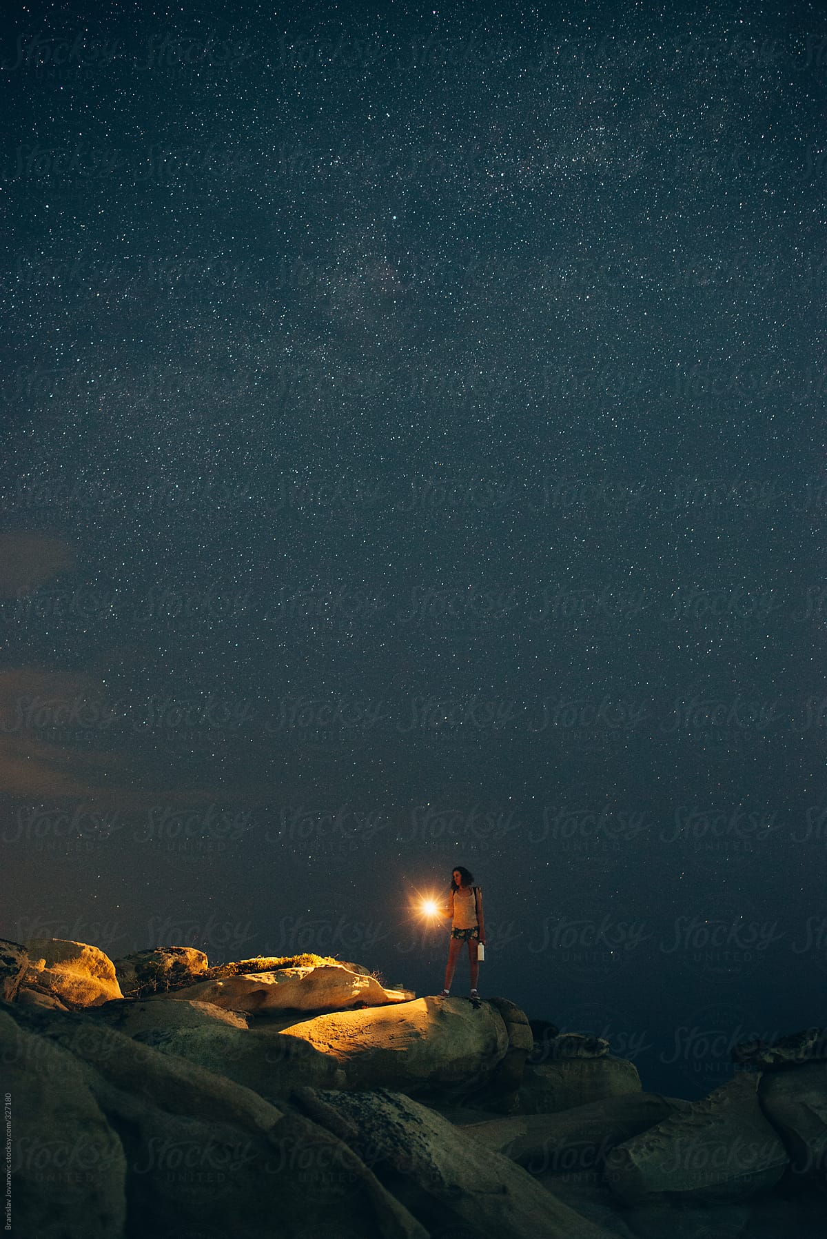Woman With Flashlight On The Rocky Beach Under The Starry Night Sky