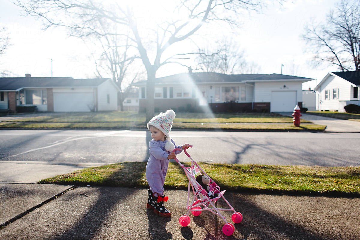 Toddler walks down sidewalk pushing doll stroller