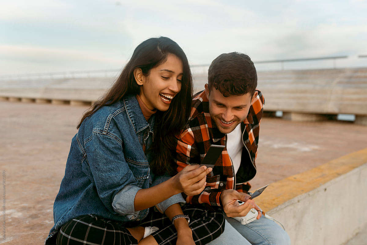 couple looking at polaroid photographs sitting on city pier