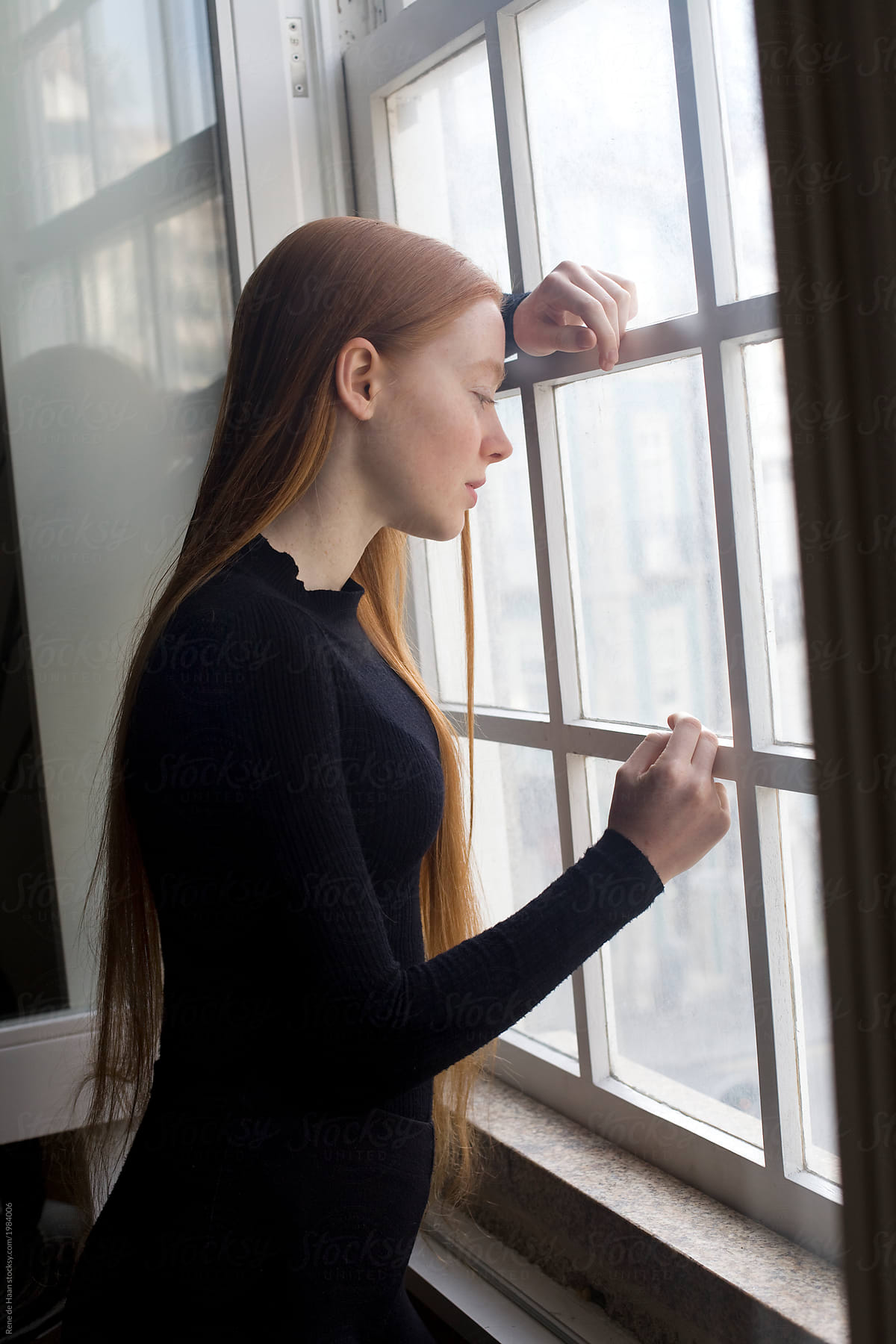 young woman standing at window, looking out