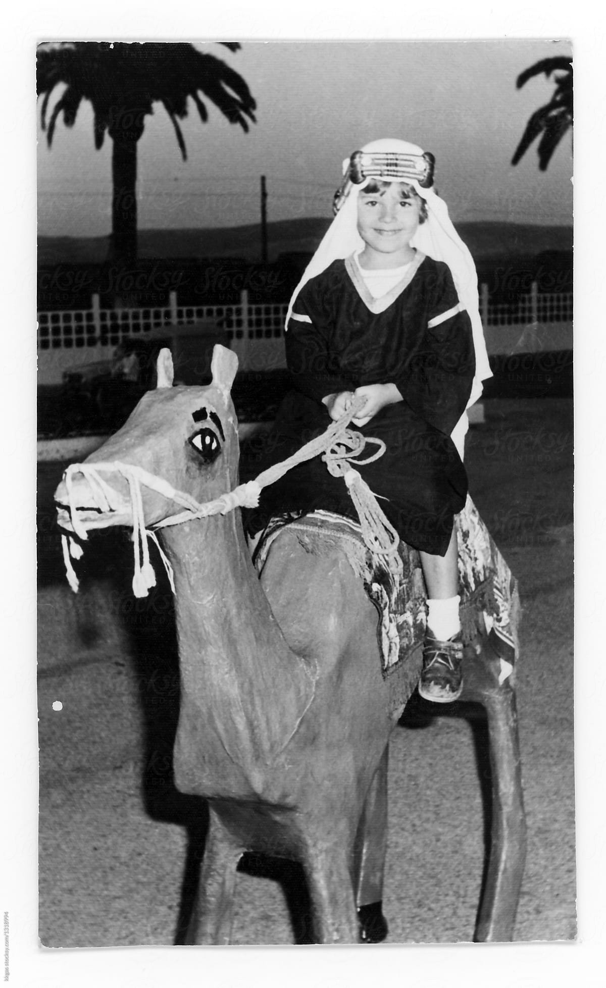 Black and white print of a little boy dressed in costume riding a toy camel