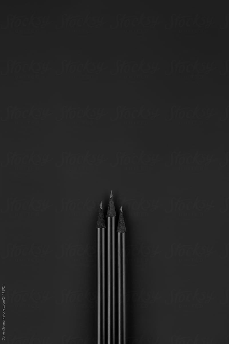 Three black pencils on a black background