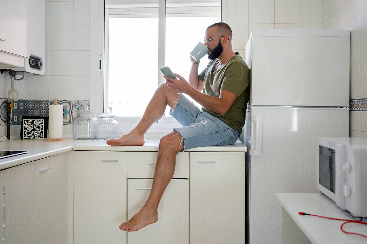 Hipster man drinking coffee and texting at kitchen