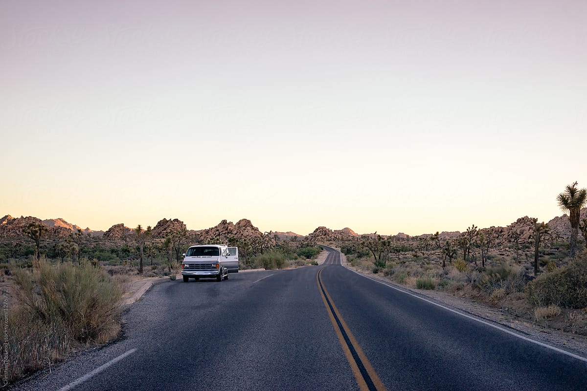 Van parked on the side of a Californian desert highway with it\'s door open.
