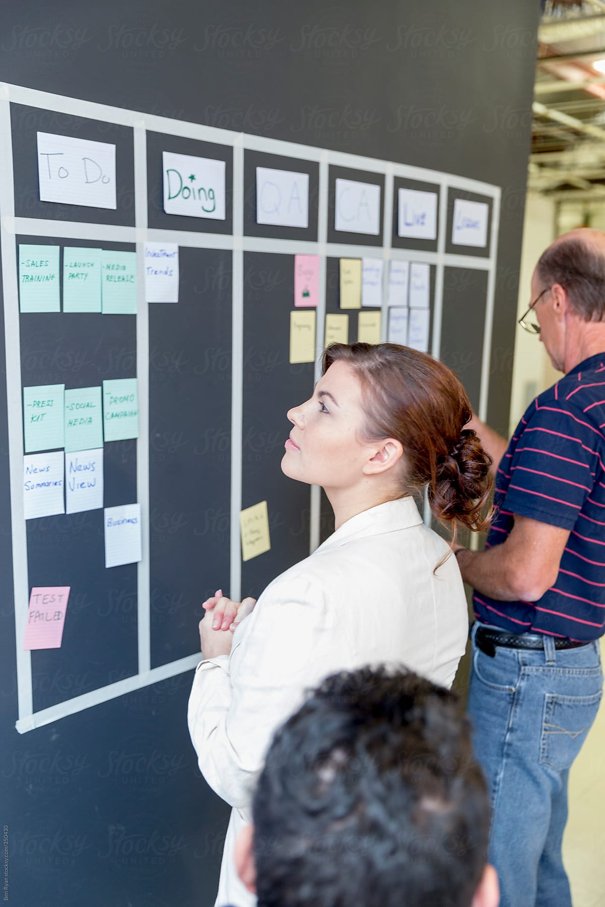 Young woman looking at agile story wall with team members working around her