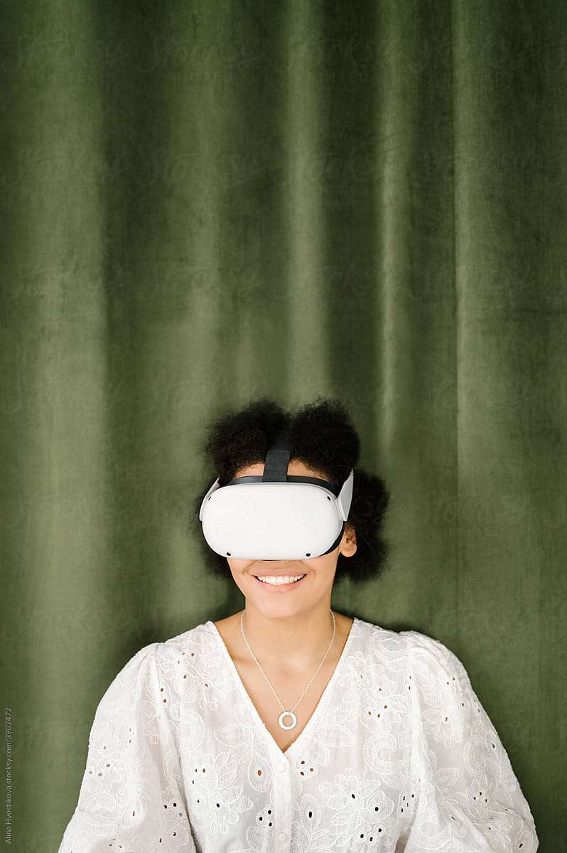 Happy black woman in VR glasses resting near green curtain