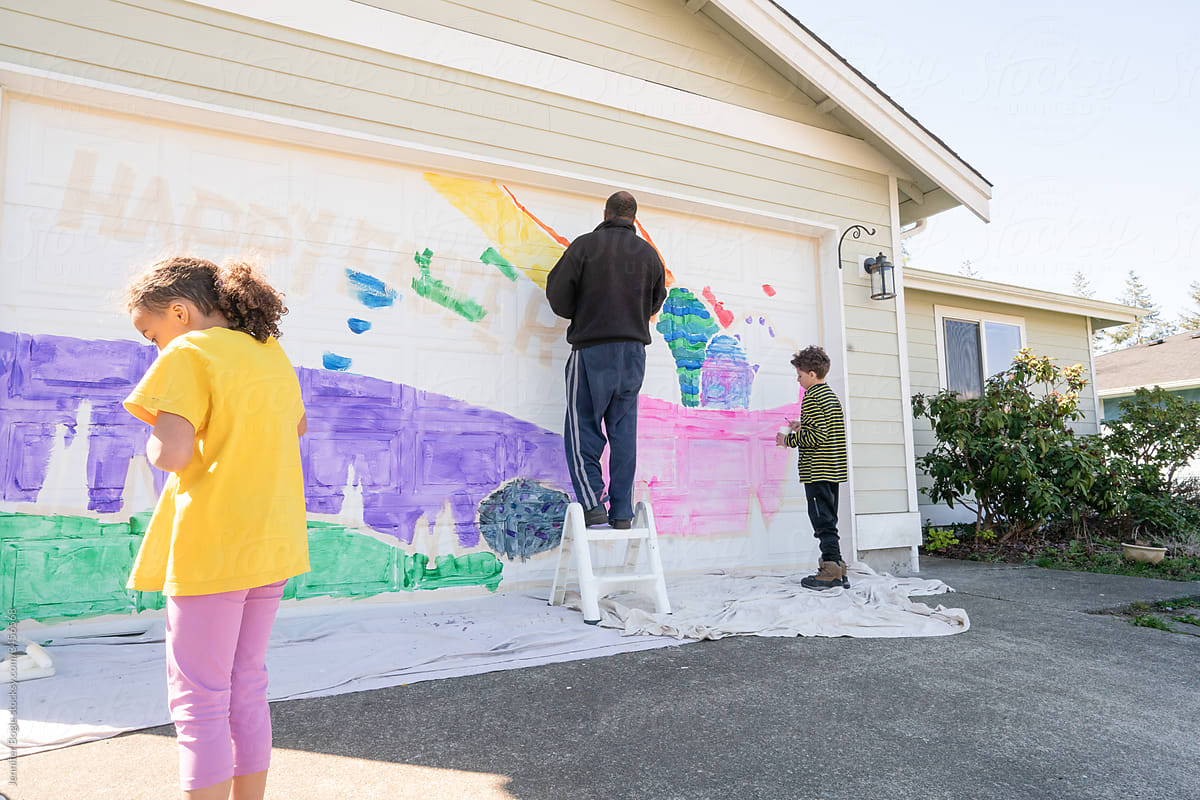 Black dad and kids painting mural on garage