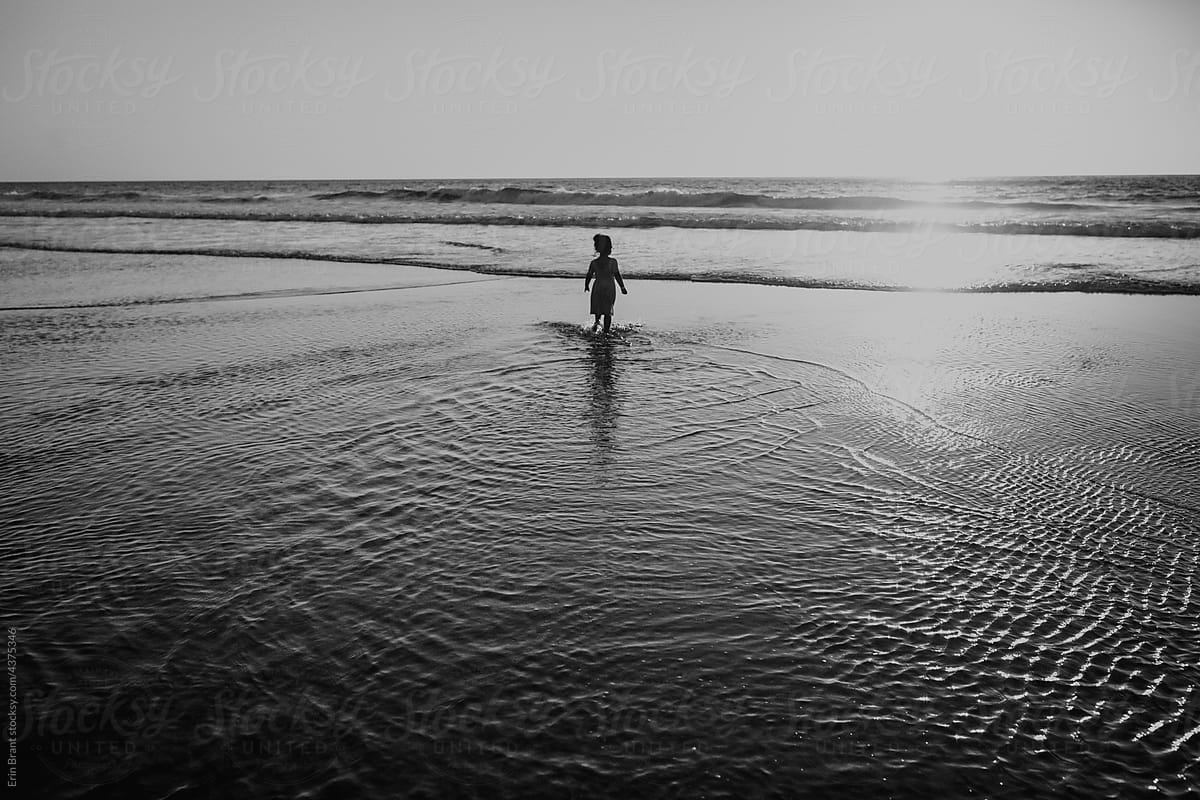Child standing in sea at sunset