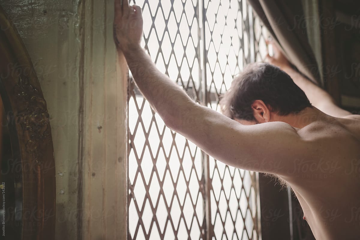 Shirtless Man Standing by Grated Window at Home