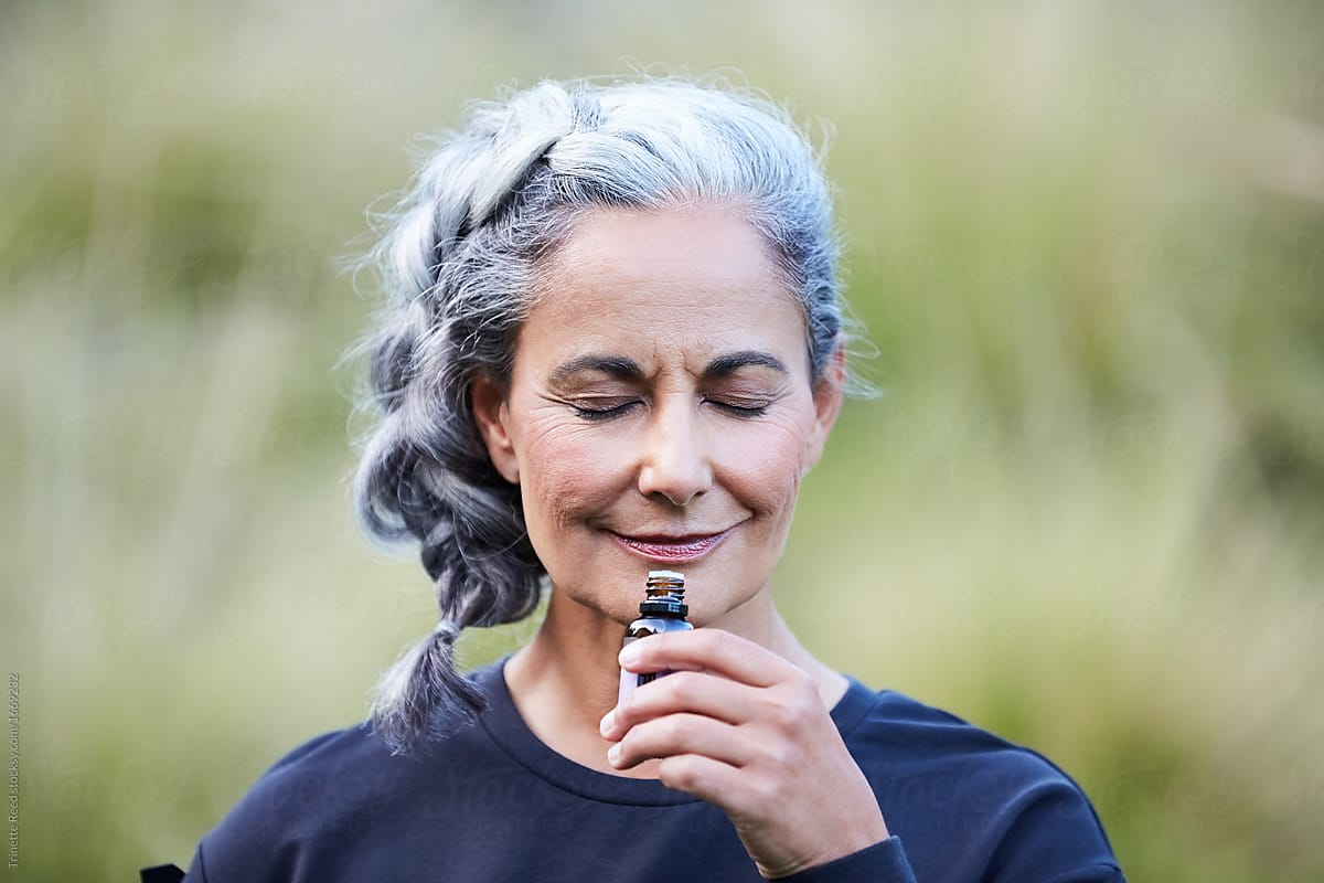 Mature woman with grey hair smelling essential oils outdoors in nature