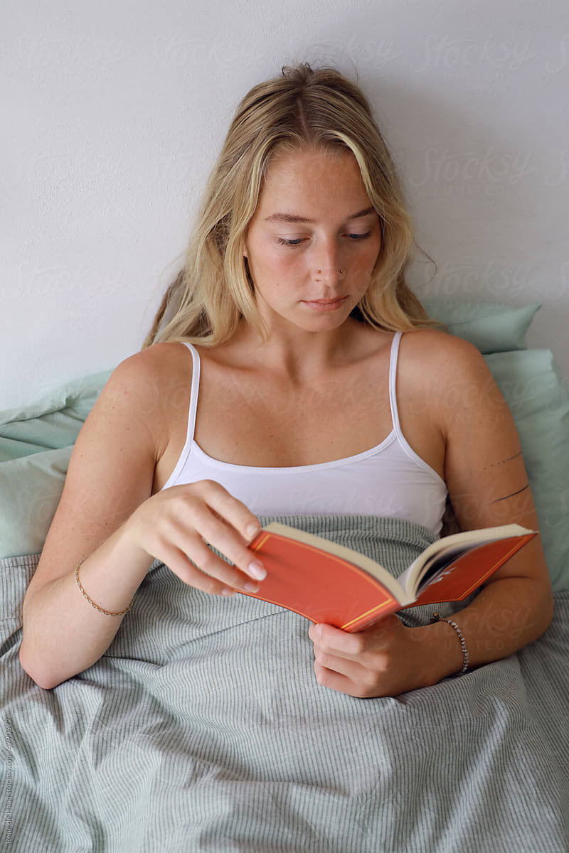 young woman reading book in bed
