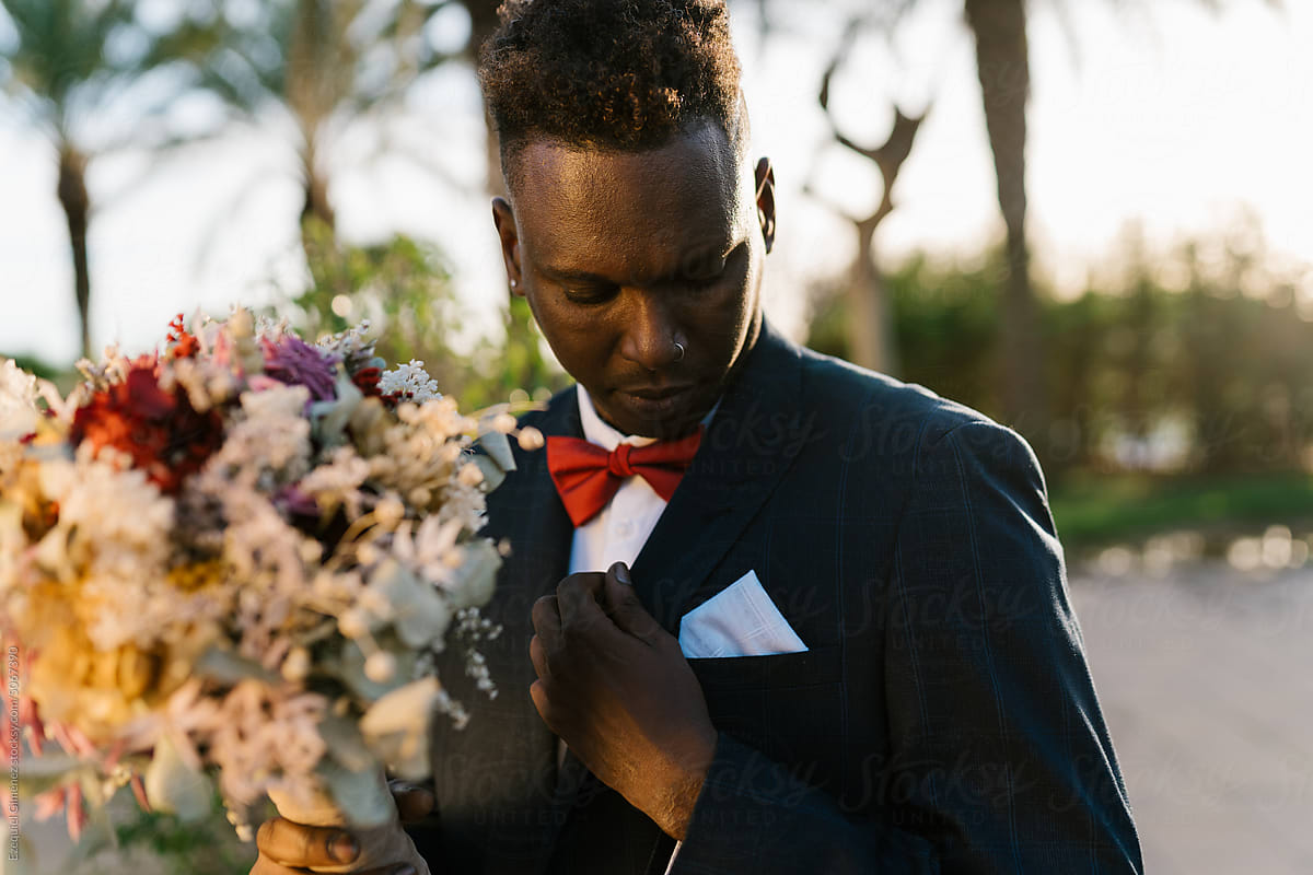 Black groom with flowers adjusting jacket