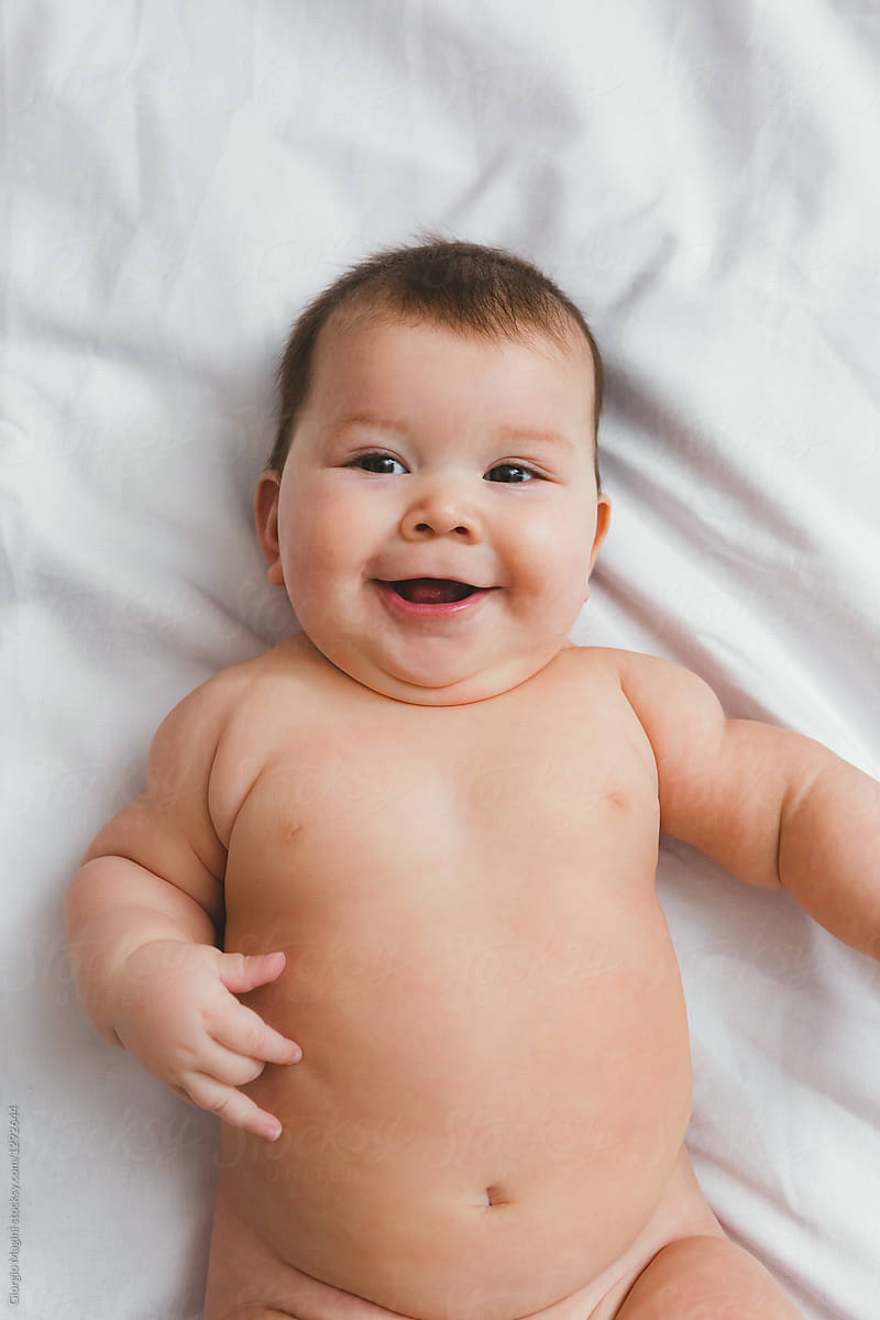 Chubby Infant Baby Nude On Bed Sheet by Giorgio Magini.