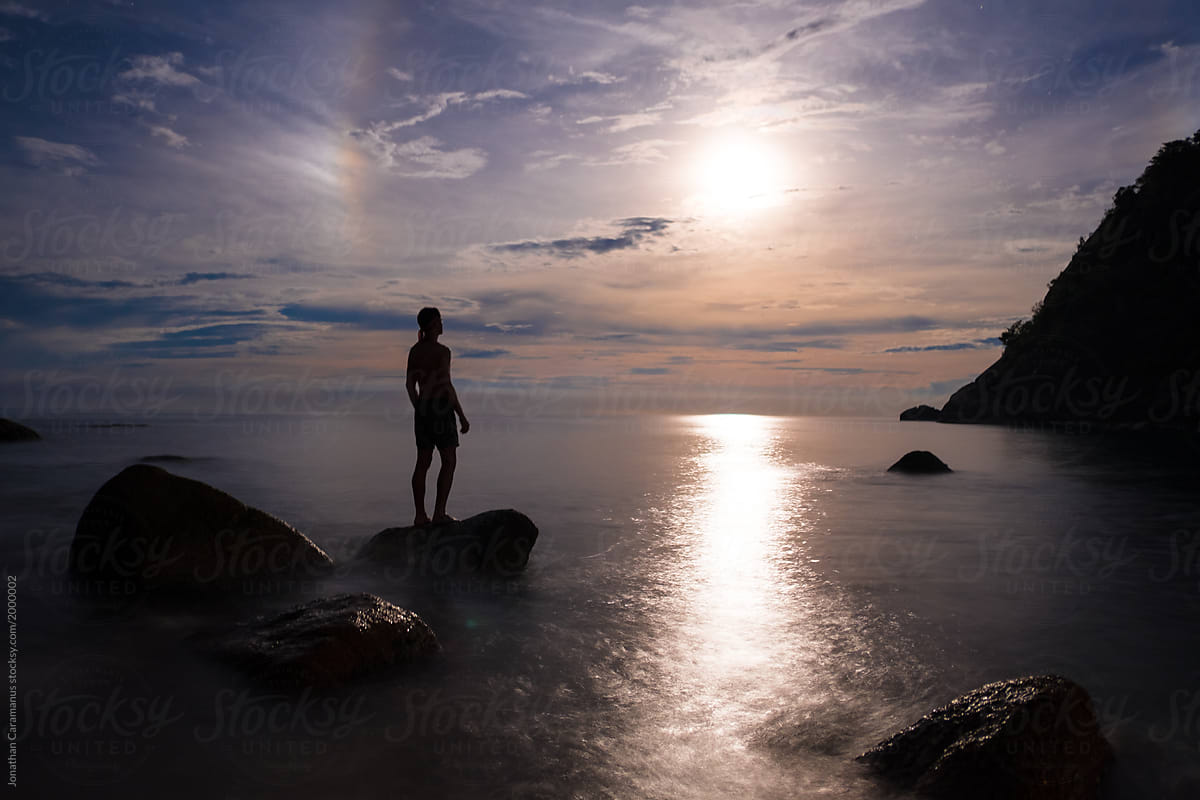 Silhouette of man standing on a rock in the ocean while looking at the rising moon