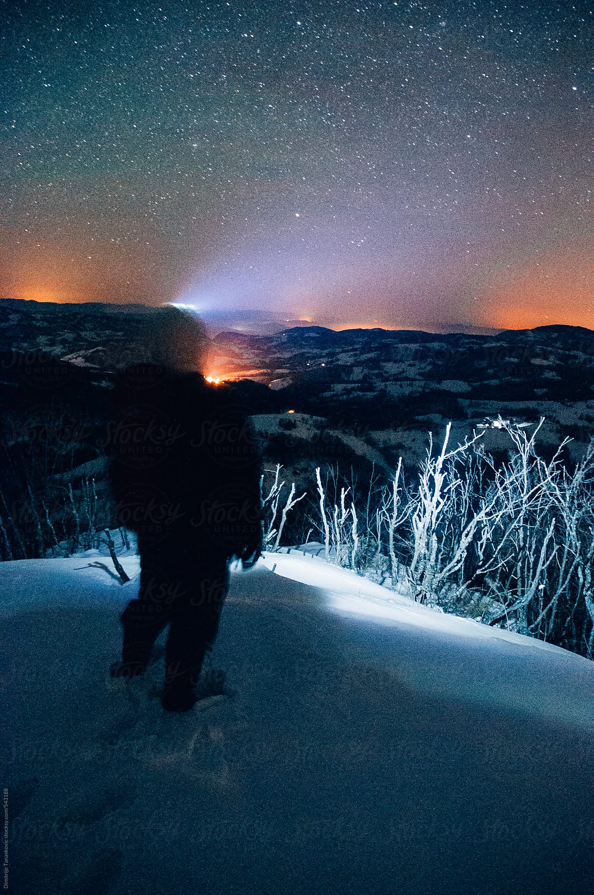 Man with headlamp standing on the mountain peak and watch at the horizon