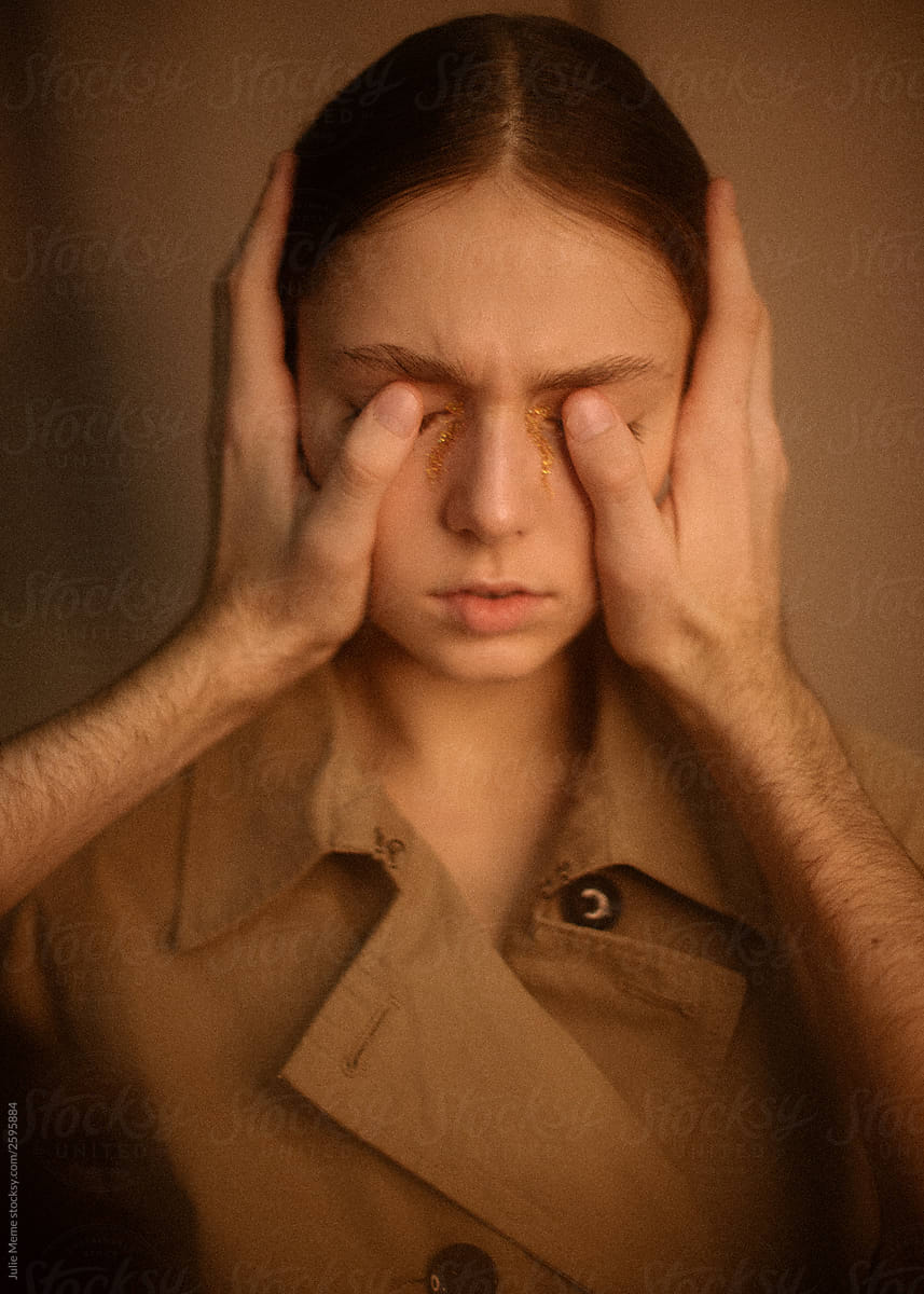 Portrait of girl in a coat with closed eyes by the hands of the man and golden tears