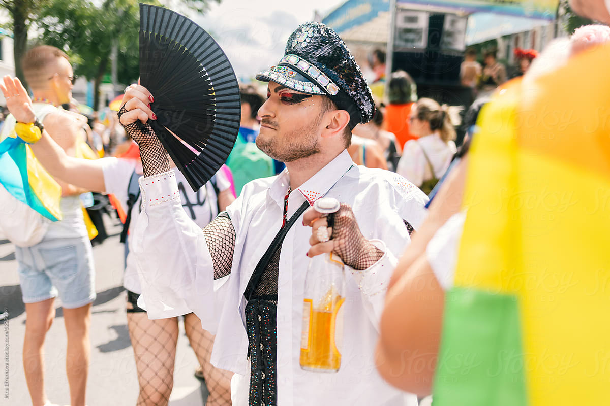 Man in Glam Make-up and Shiny Officer Hat and hand fan at Pride