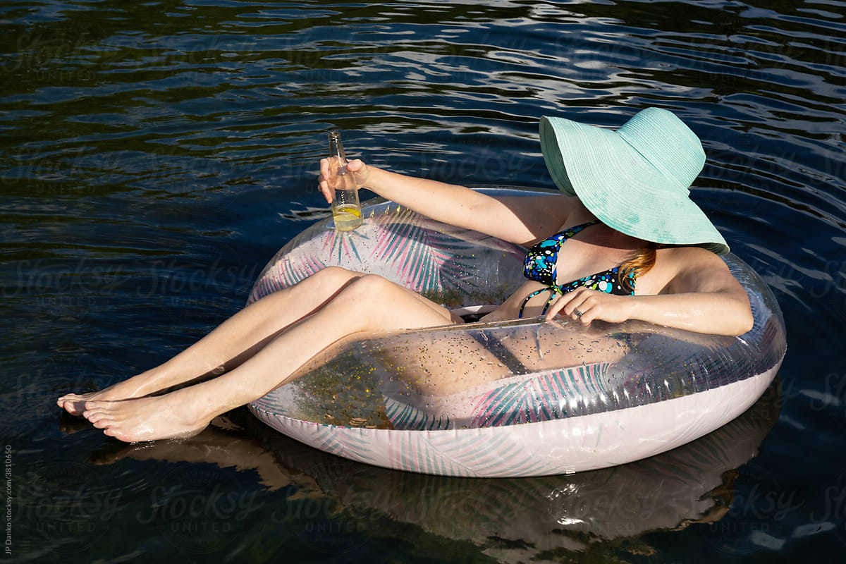 Woman Floating on Tube Relaxing with Drink on Sunny Summer Day at Cottage Lake
