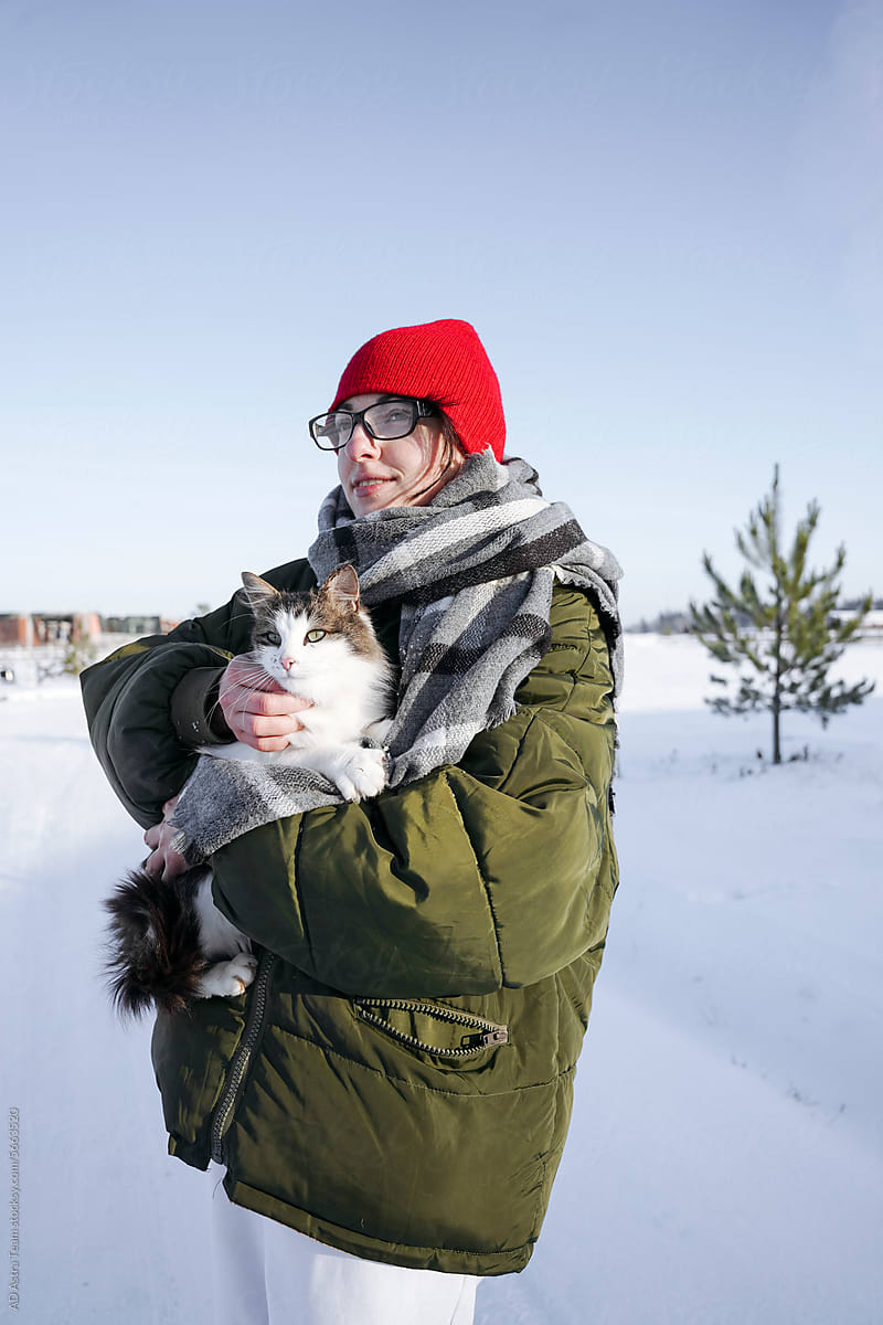 A happy woman holds a cat in her arms in winter