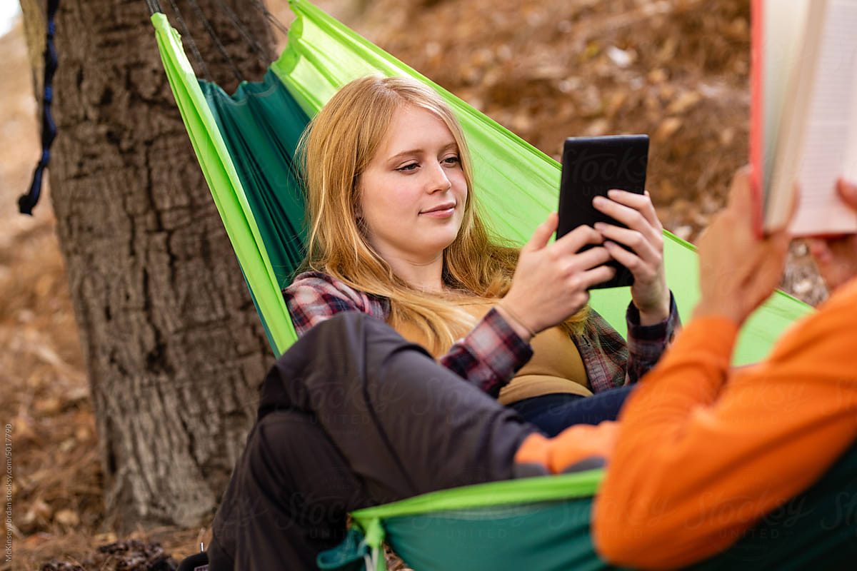 Two Hikers Read Together While Sitting On A Hammock