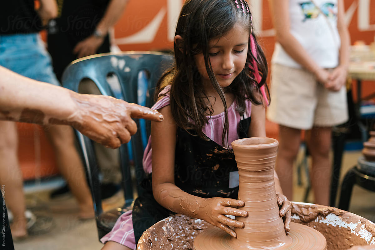Faceless person pointing near girl making clay vessel