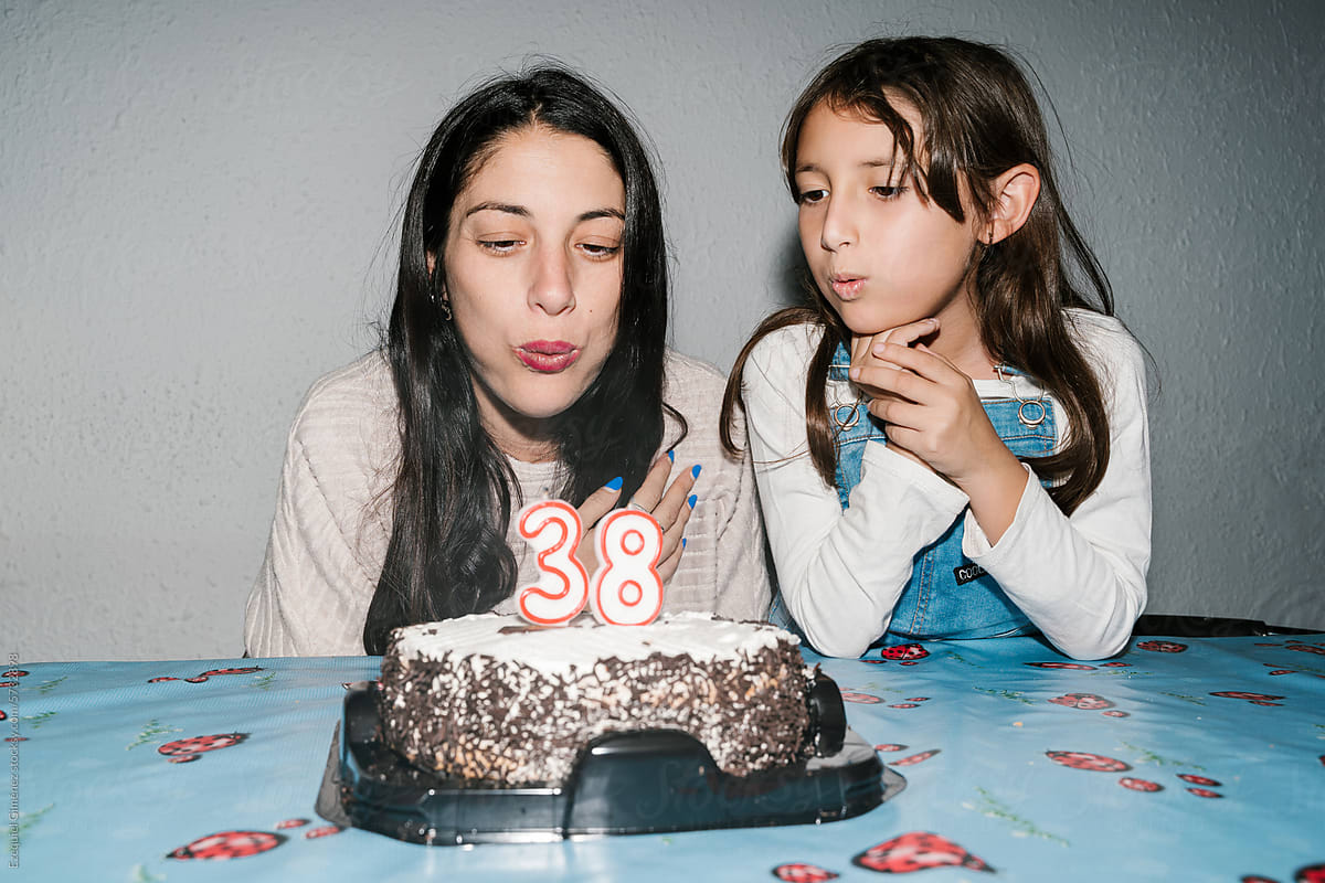 Smiling young mother blowing candles on cake with daughter