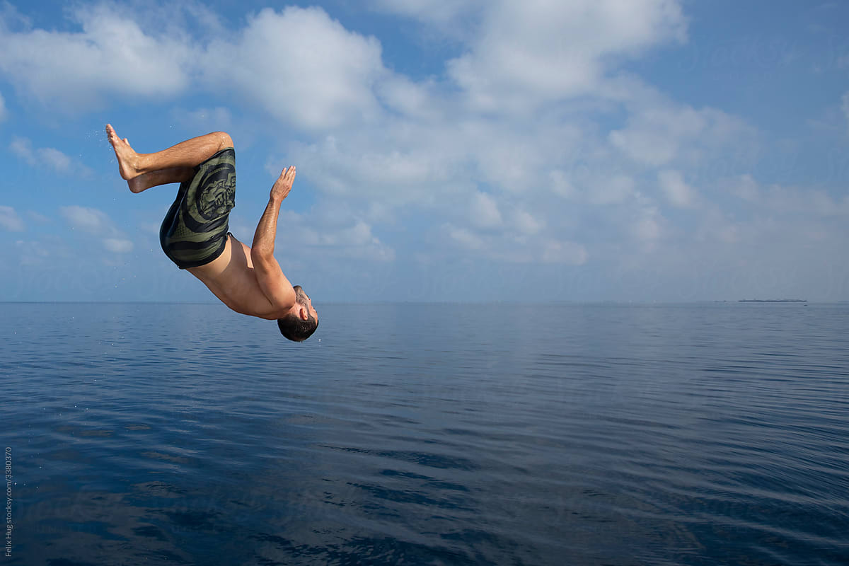 A man doing a backflip into the blue ocean