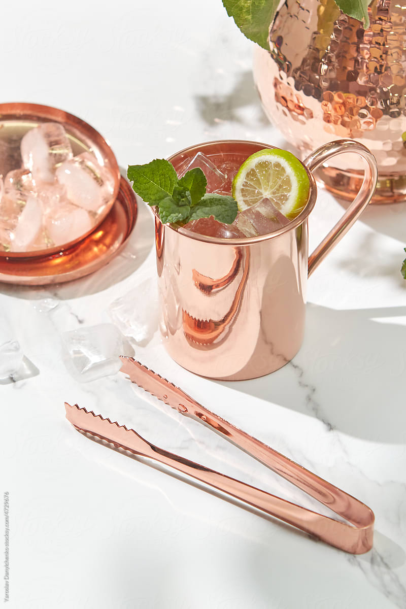 Copper cup of lemonade, jug and tongs on marble surface.