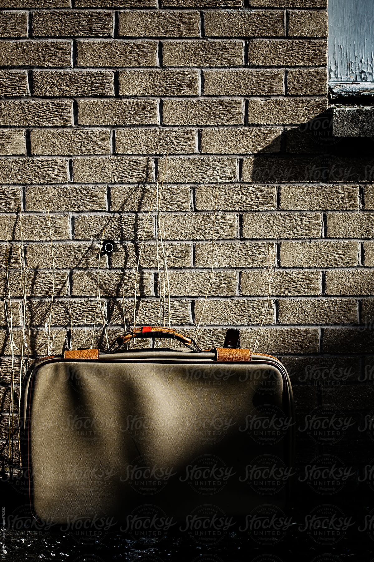 Old retro suitcase left in the shadows against a brick wall.