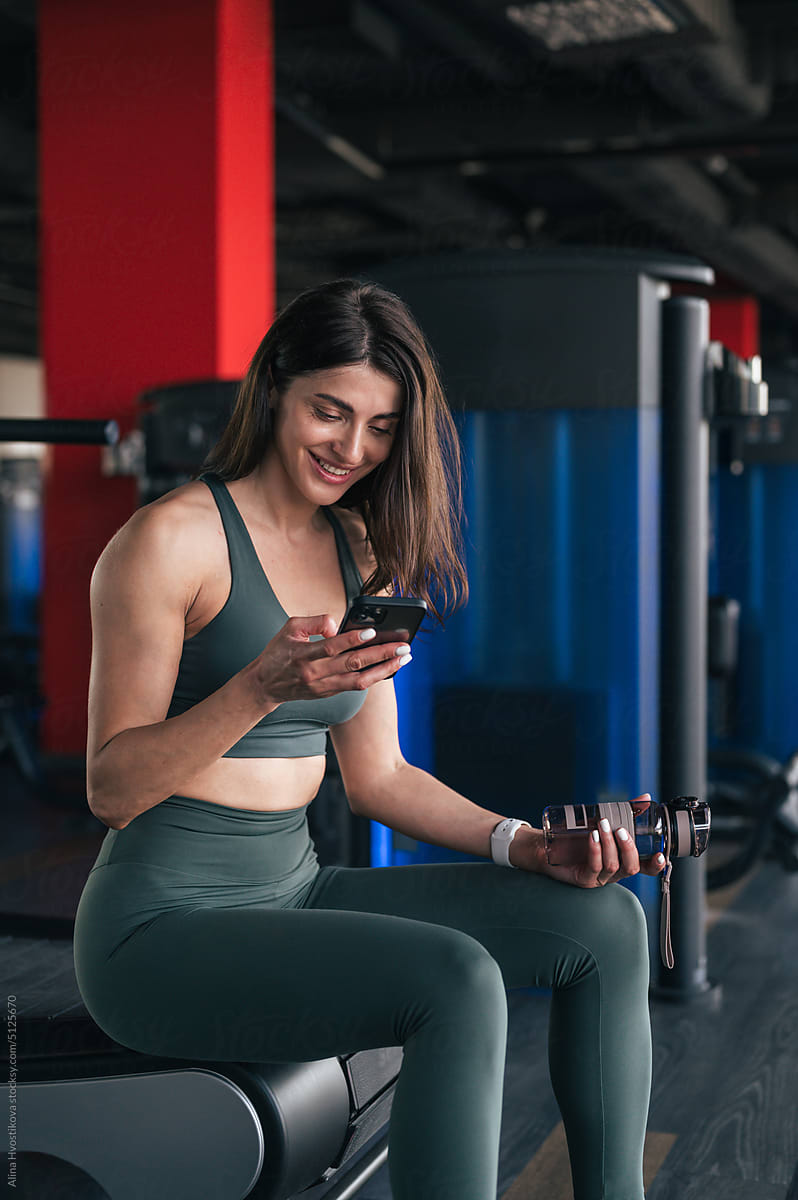 Smiling sportswoman browsing smartphone in gym