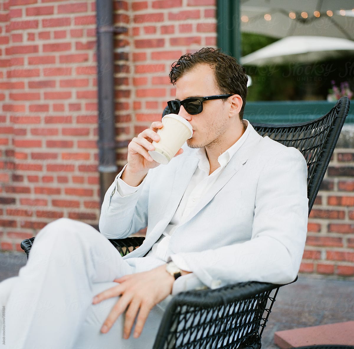 Attractive man in a suit drinking a cup of coffee on a patio