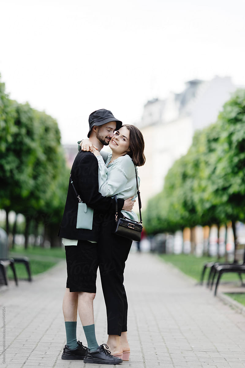Stylish lovers hugging and posing on road, surrounded by green trees